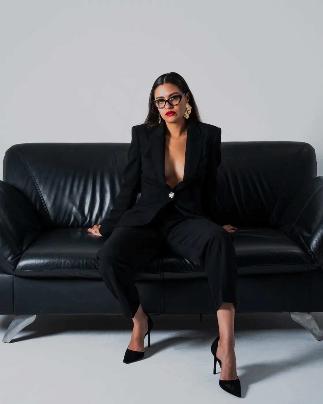 Seated on a black leather sofa in a black suit