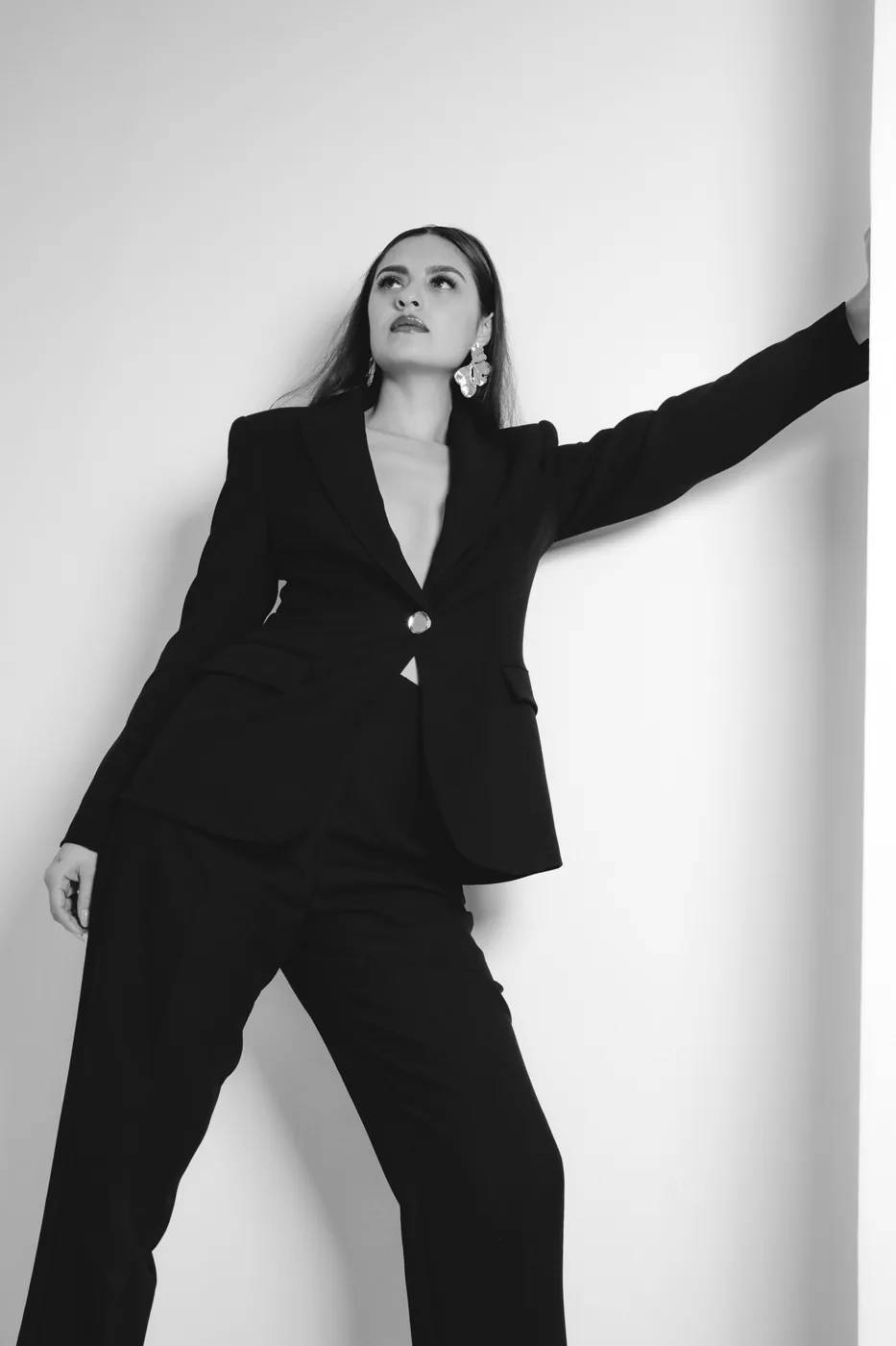 Standing against a white wall in a black suit